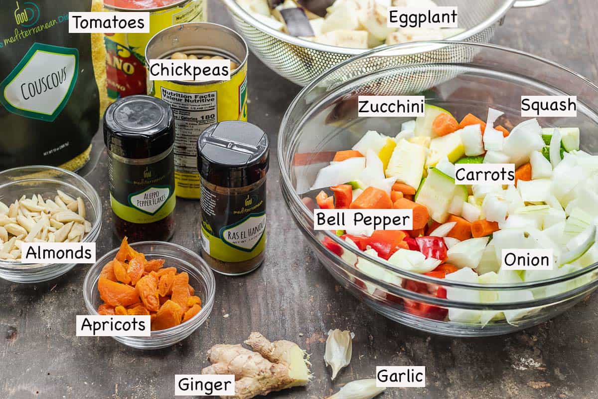 labeled ingredients for vegetable couscous including a medley of vegetables, chickpeas, canned tomatoes, couscous, almonds, dried apricots, ginger, garlic, ras el hanout, and Aleppo-style pepper
