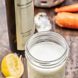 creamy feta dressing in a mason jar with olive oil, lemon, and vegetables in the background.