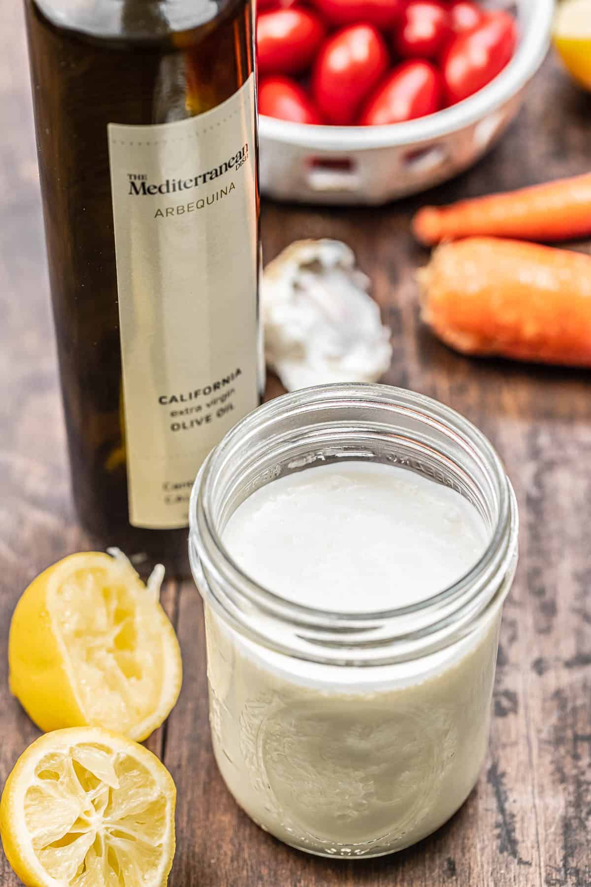 creamy feta dressing in a mason jar with olive oil, lemon, and vegetables in the background.