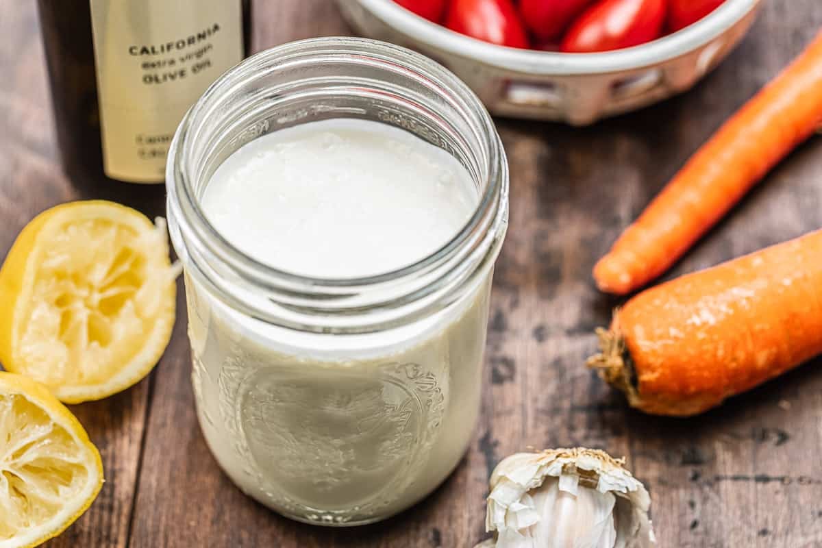 homemade feta dressing with EVOO, garlic, lemons, and vegetables in the background.