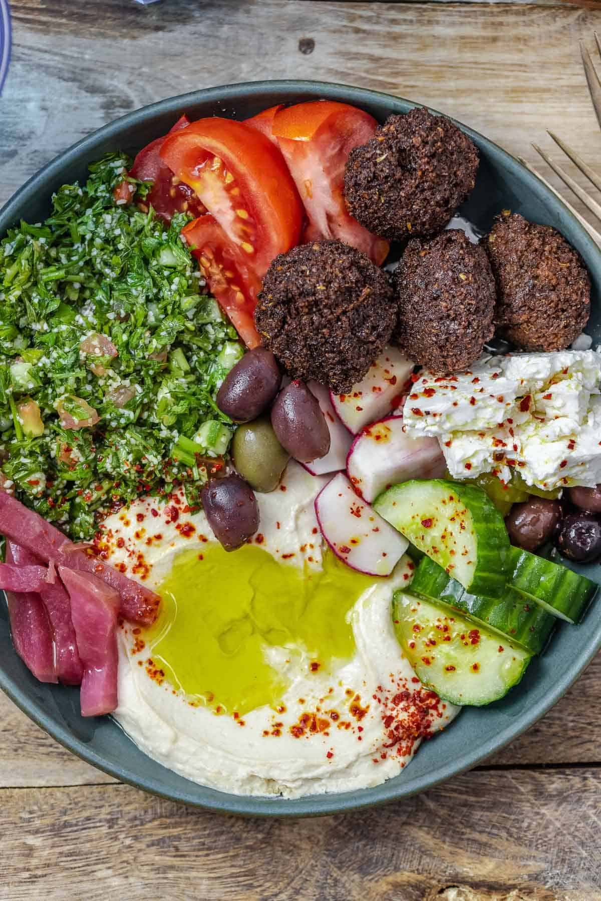 A big Mediterranean falafel bowl assembled with hummus, pickles, olives , fresh vegetables and a tabouli salad