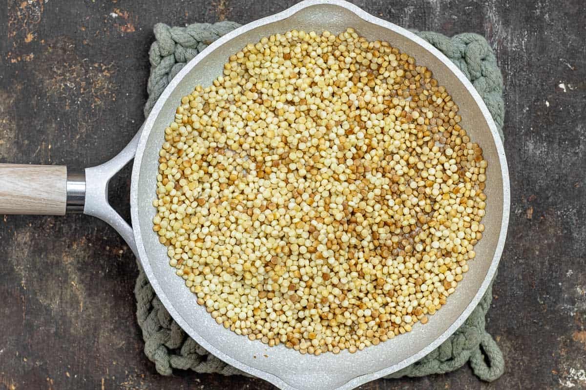 Isreali couscous toasting in a non-stick skillet.