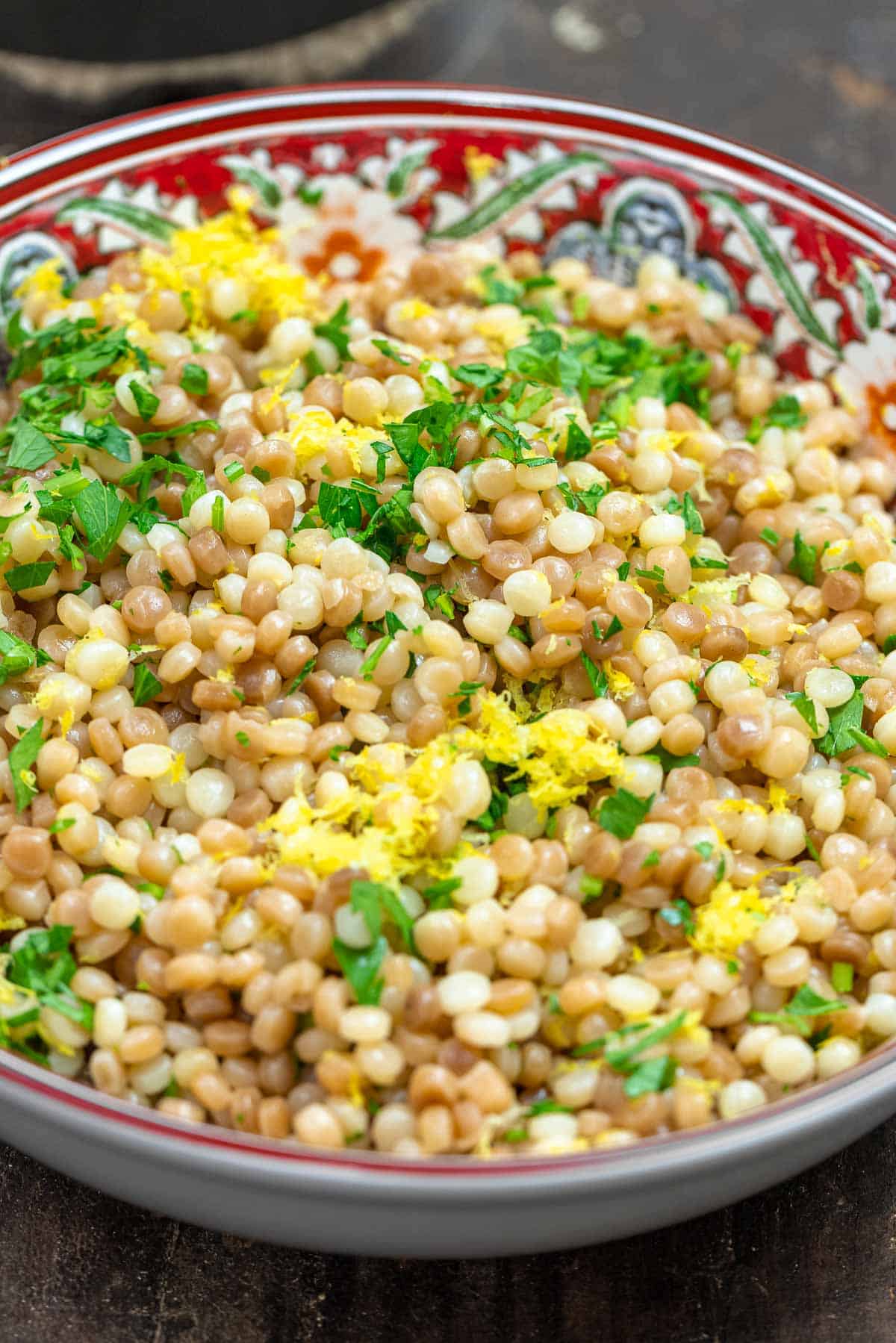 Israeli couscous with fresh herbs and lemon zest in a bowl.