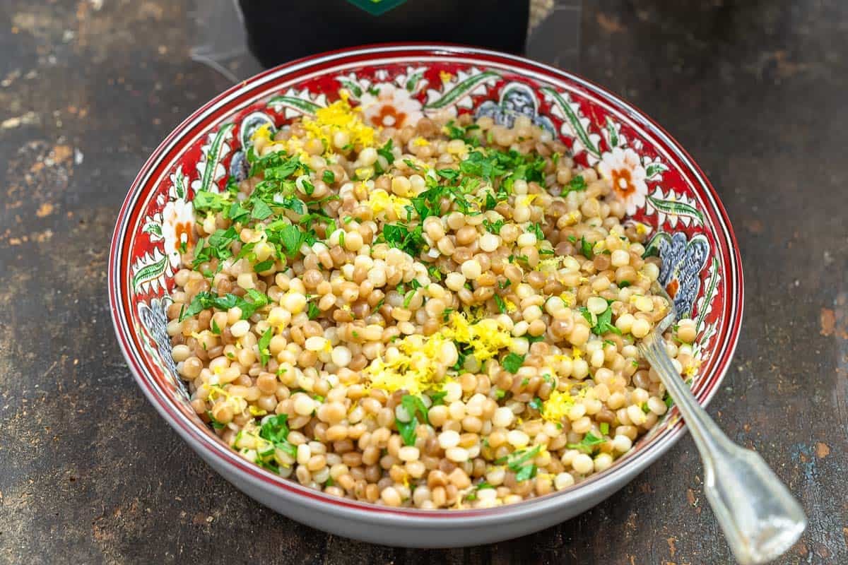 Pearl couscous in a patterned bowl with fresh herbs and lemon zest.