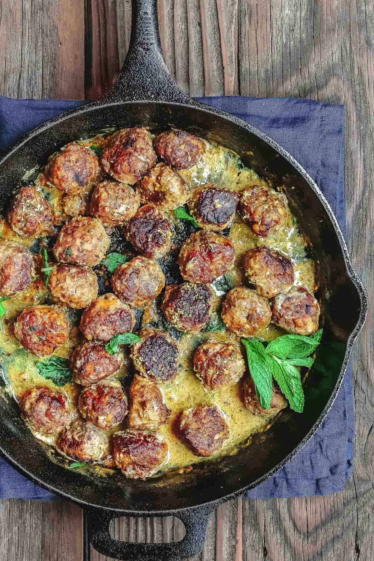 Keftedes in a cast-iron skillet with a lemon and herb sauce.