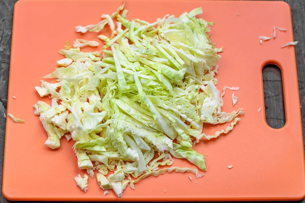 shredded cabbage on an orange cutting board.