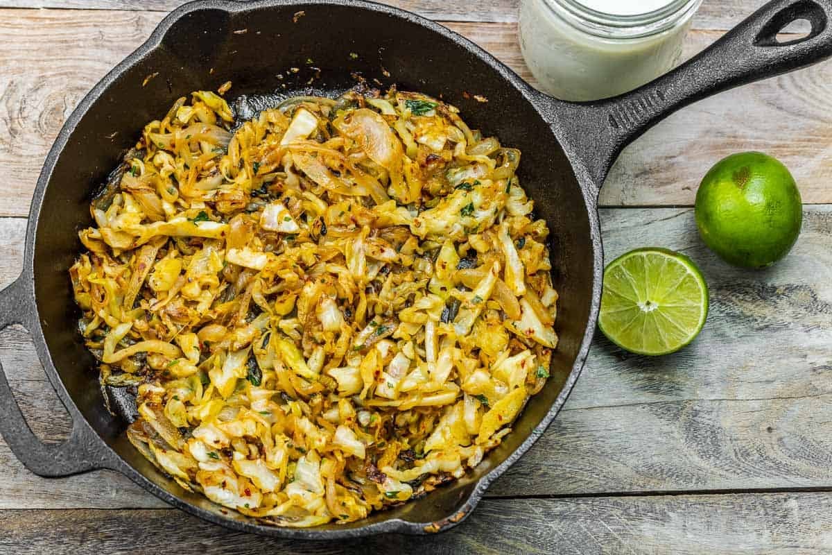 sauteed cabbage on a wooden table with lime and dressing to the side.