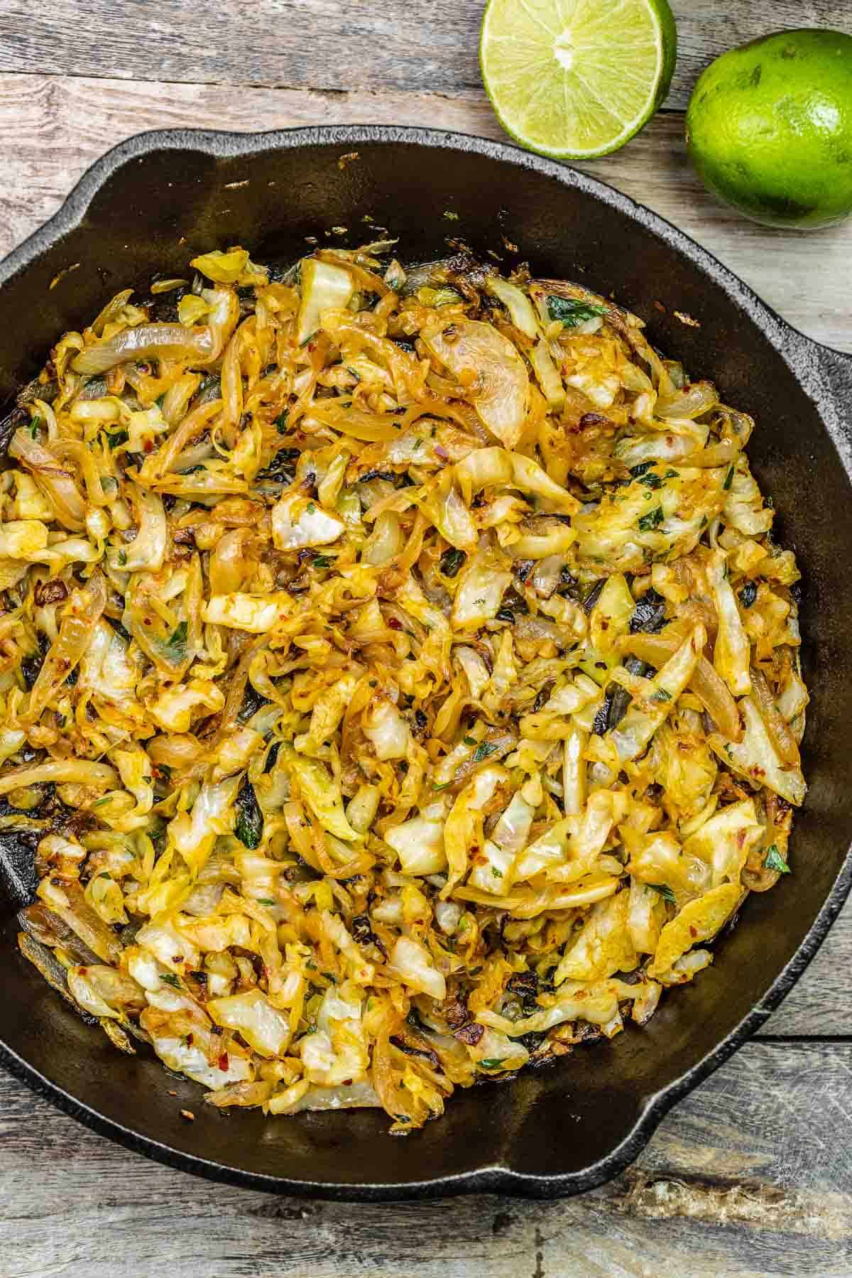 sauteed cabbage in a cast iron skillet with lime on the side.