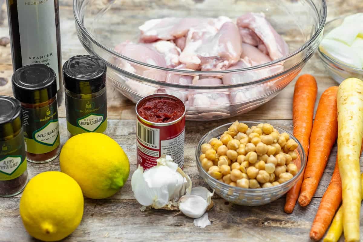 ingredients for sheet pan chicken with chickpeas including tomato paste, chicken thighs, carrots, chickpeas, garlic, lemons, olive oil, and spices.