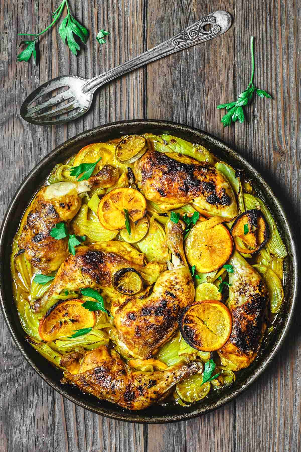 turmeric chicken in a baking dish after roasting, with a slotted spoon to the side.