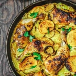 turmeric roasted chicken with fennel and citrus on a wooden table with a silver spoon to the side.