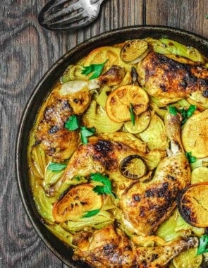 turmeric roasted chicken with fennel and citrus on a wooden table with a silver spoon to the side.