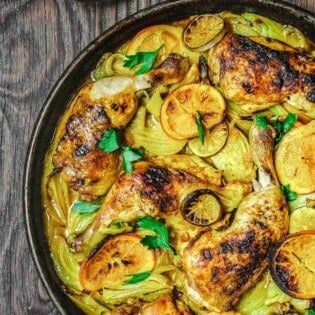 turmeric roasted chicken with fennel and citrus on a wooden table with a silver spoon to the side.