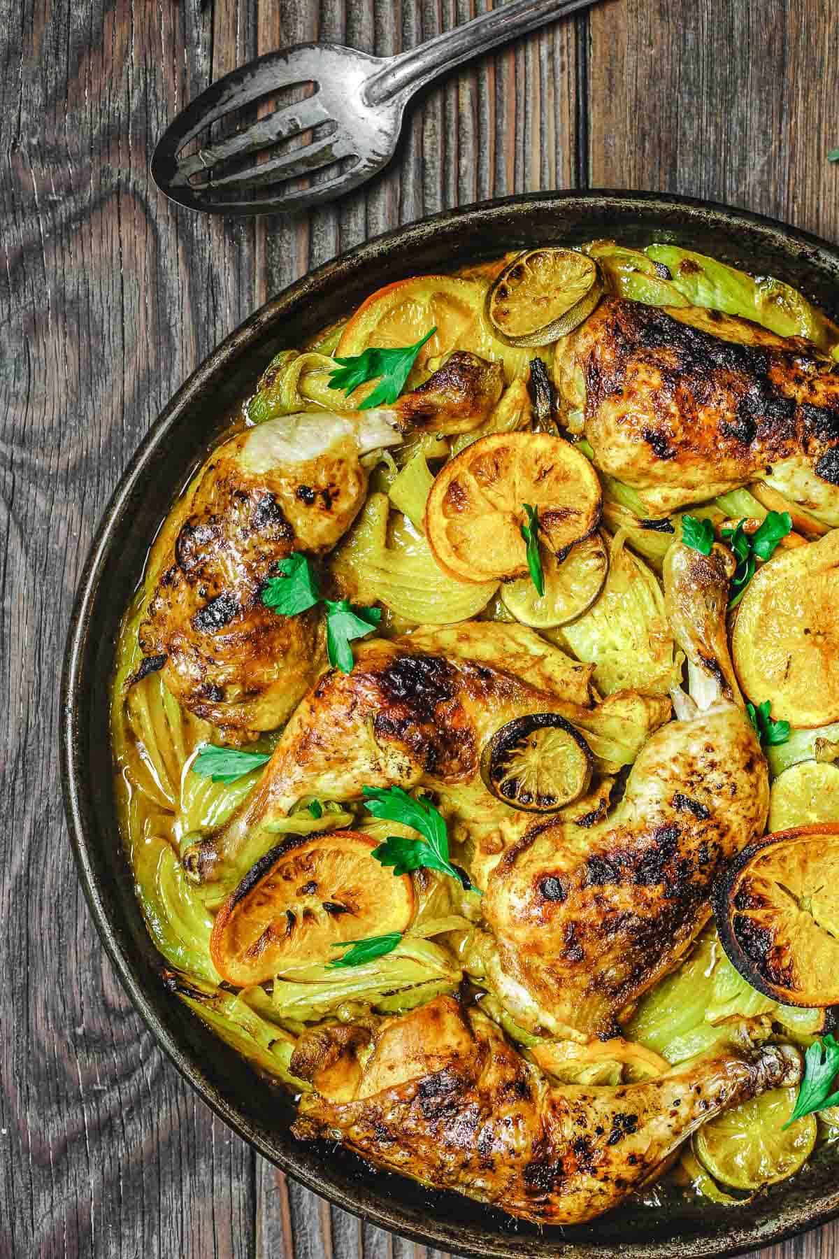 turmeric roasted chicken with fennel and citrus on a wooden table with a silver spoon to the side.