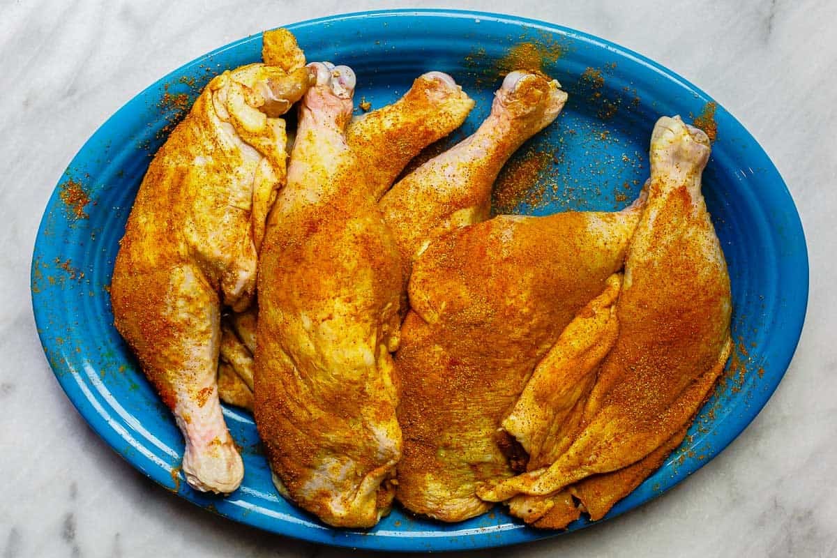 marinated chicken leg quarters on a blue platter.