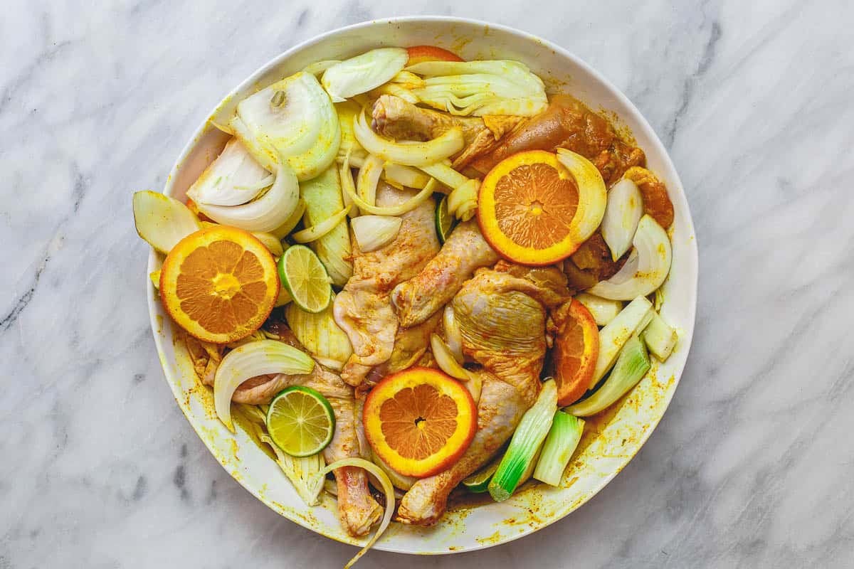 marinated chicken legs combined with fennel, onions, lime, and oranges in a large white bowl.