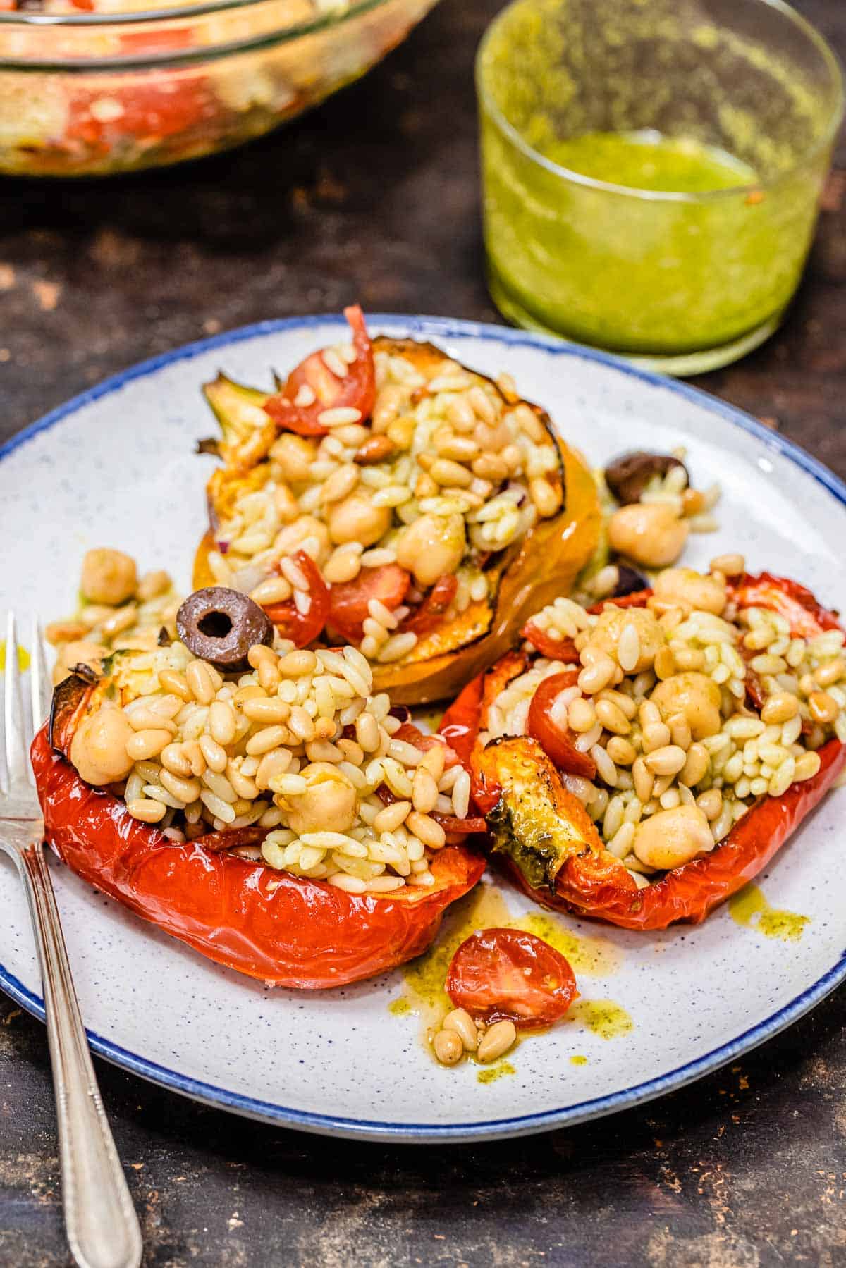 vegetarian stuffed peppers on a blue and white plate with a fork. A glass container of basil vinaigrette is in the background.