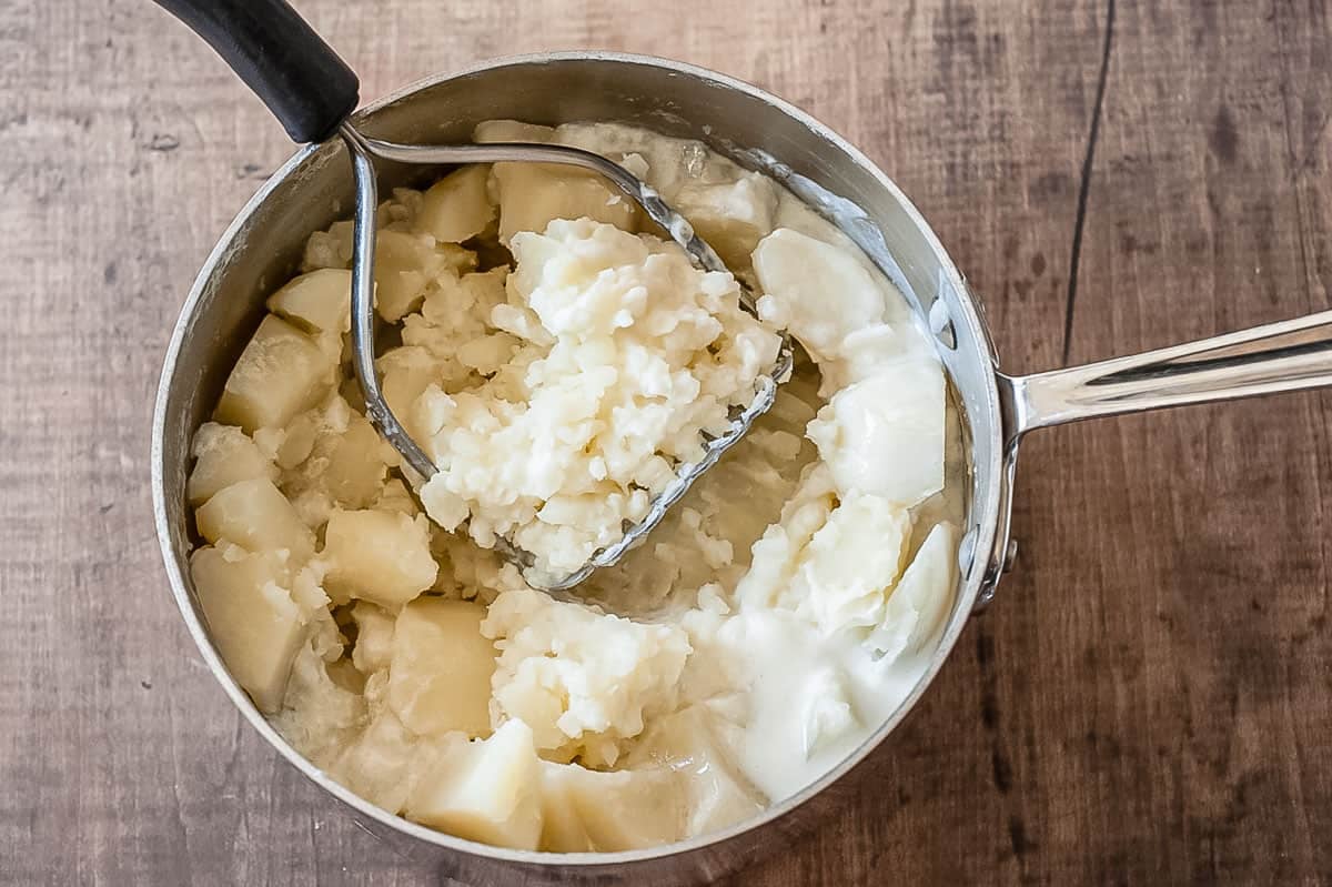 Cubes of potatoes being mashed in a saucepan