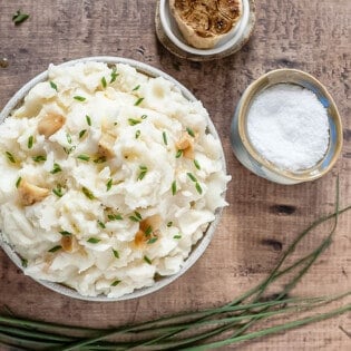 A bowl of mashed potatoes with roasted garlic, salt and chives