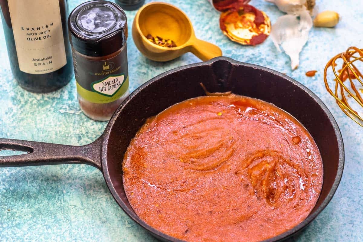 bravas sauce in a small pan with olive oil, smoked paprika, and red pepper flakes in the background.