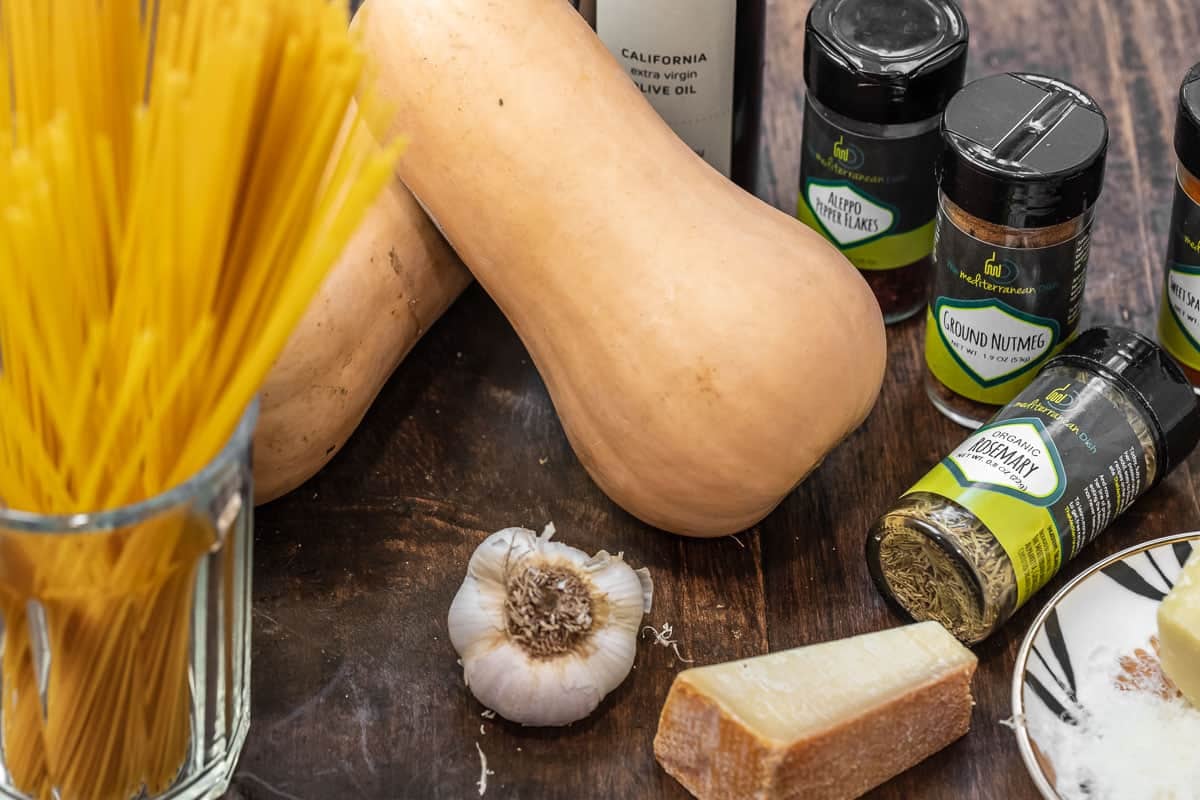 ingredients for butternut squash pasta including squash, pasta, olive oil, garlic, cheese, and herbs and spices.