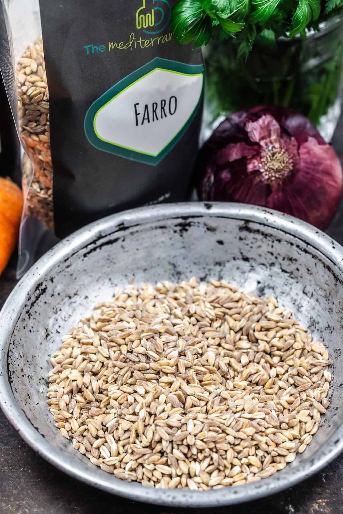 close up of uncooked farro in a bowl, with The Mediterranean Dish farro in the background.