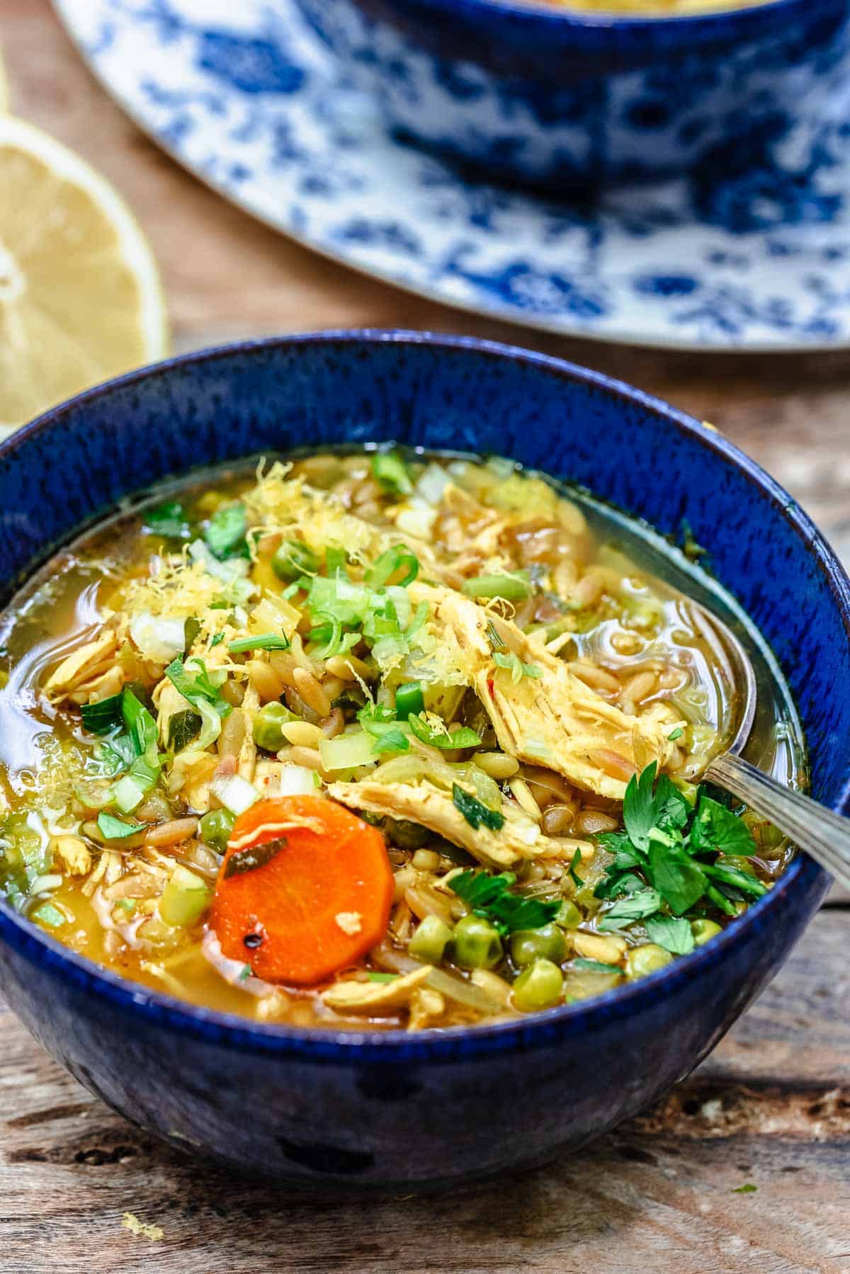 Lemon Chicken Orzo Soup in a blue bowl with a spoon in it.