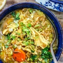 Lemon chicken orzo soup in a blue serving bowl with a spoon.