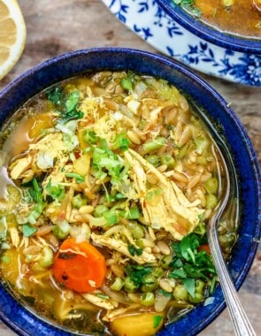 Lemon chicken orzo soup in a blue serving bowl with a spoon.