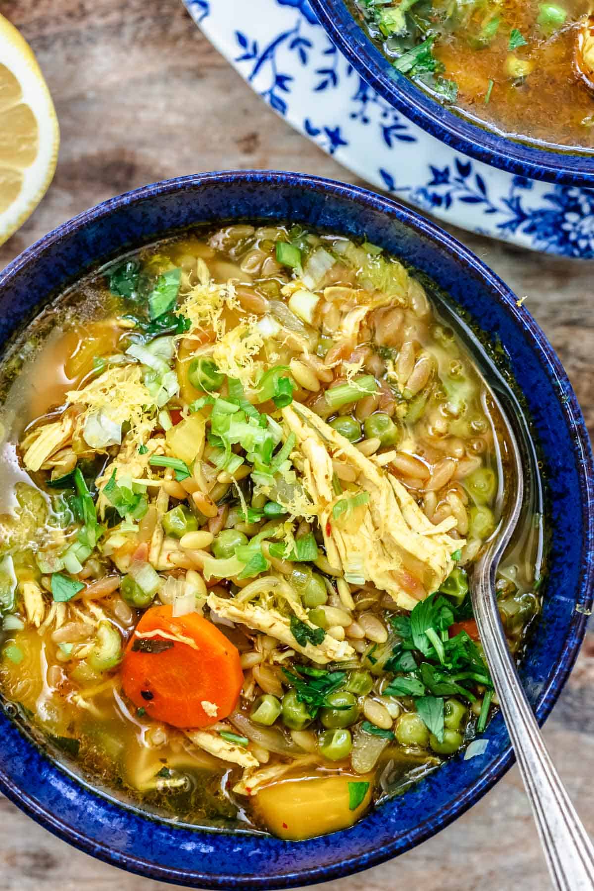 Lemon orzo chicken soup in a blue serving bowl with a spoon.