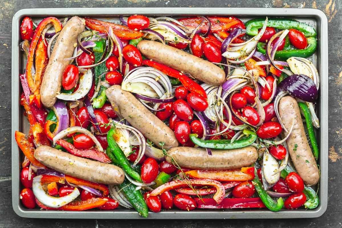 saucisses et légumes sur une plaque à pâtisserie prêts à griller.
