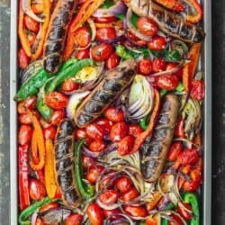 sheet pan sausage and peppers in the oven on a wooden surface.