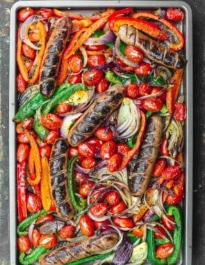 sheet pan sausage and peppers in the oven on a wooden surface.