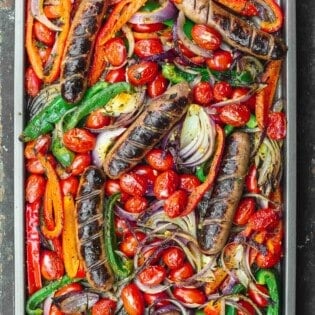 sheet pan sausage and peppers in the oven on a wooden surface.