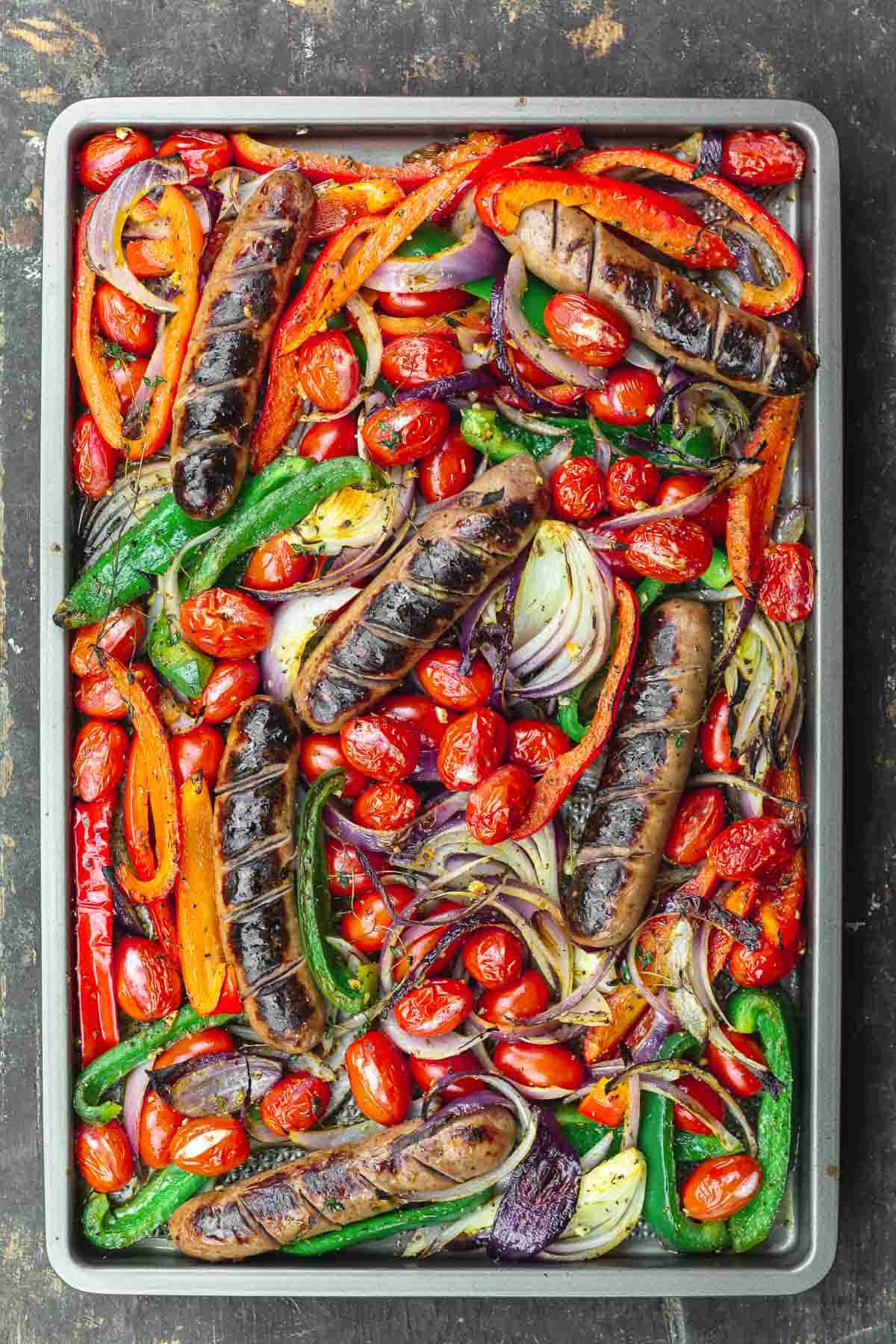 sheet pan sausage and peppers in the oven on a wooden surface.