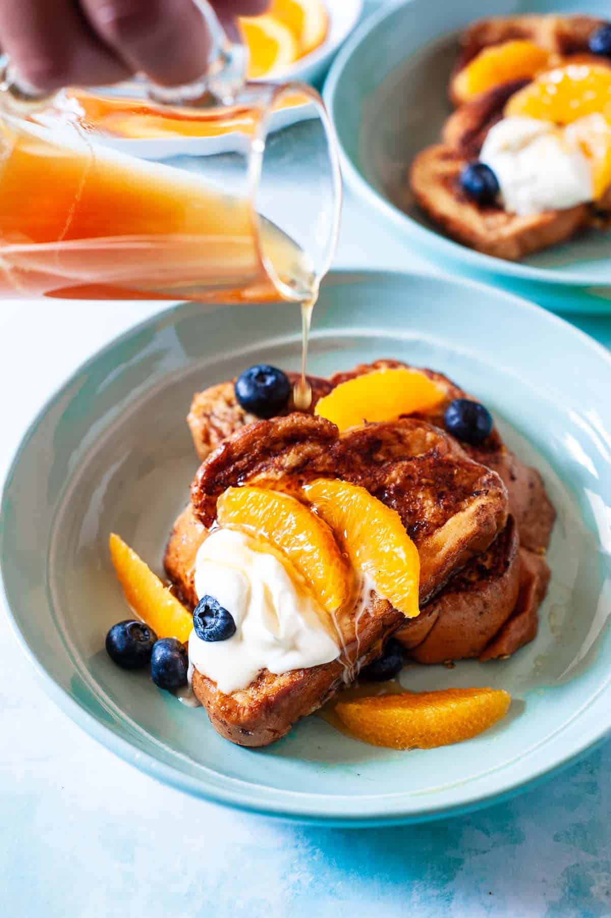 orange honey syrup being poured on a slice of challah french toast.