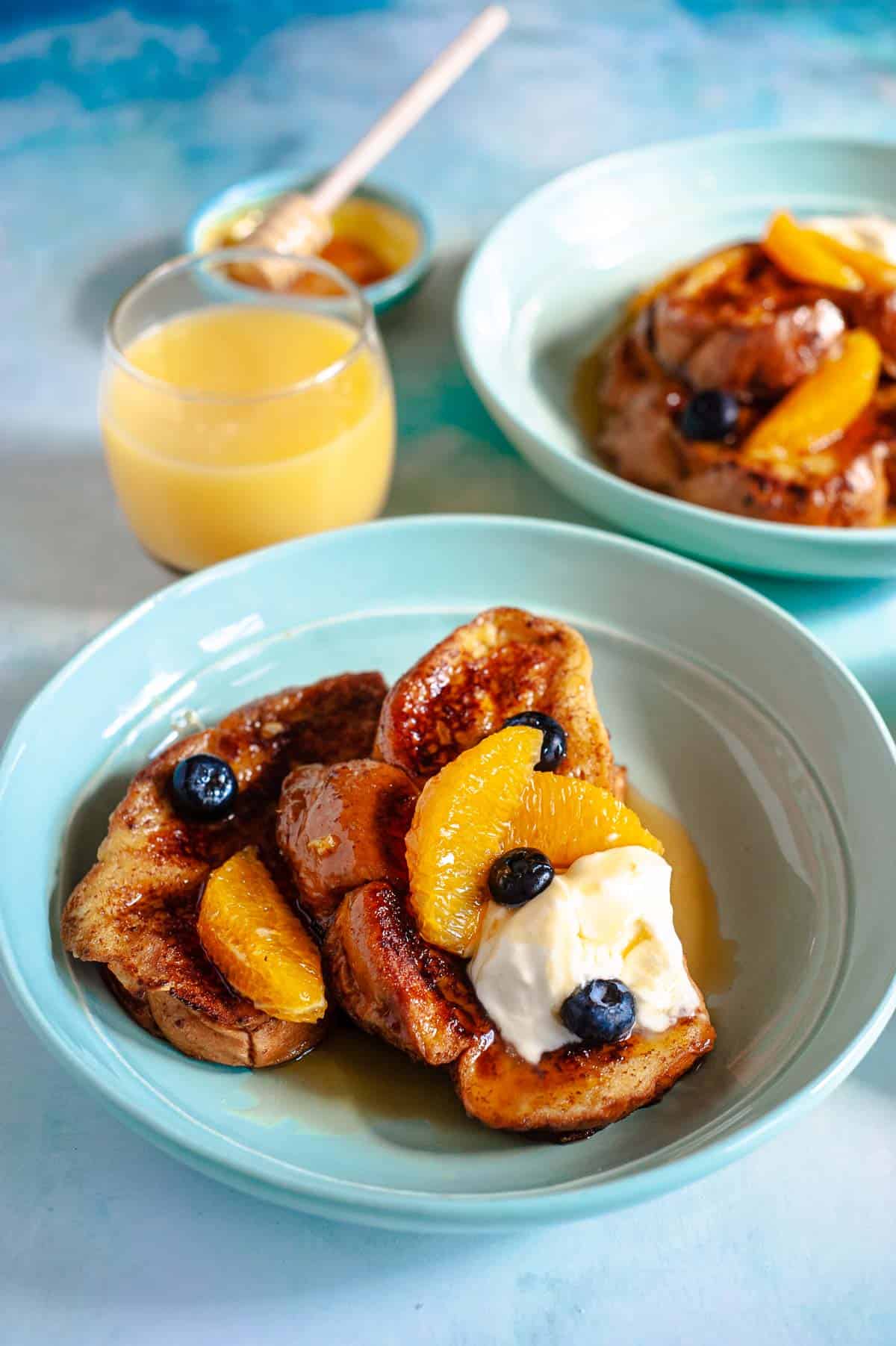 a plate of challah french toast topped with blueberries, orange slices and creme fraiche and a glass of orange juice..