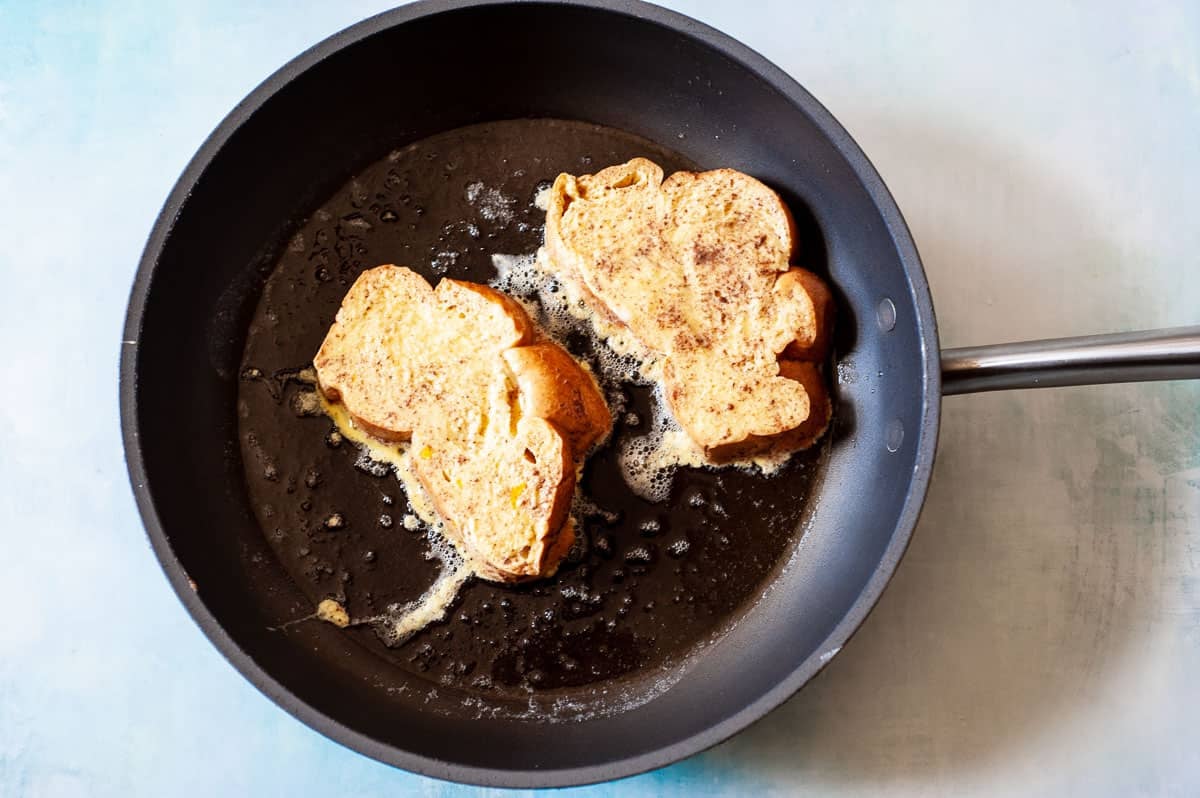 two slices of challah heating in a skillet.