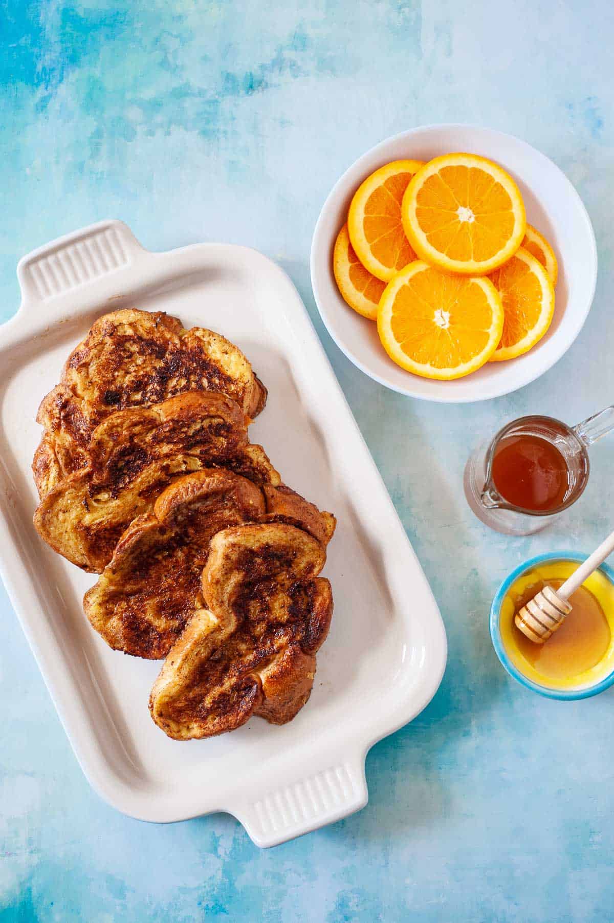 slices of challah french toast with a bowl of sliced oranges and honey.
