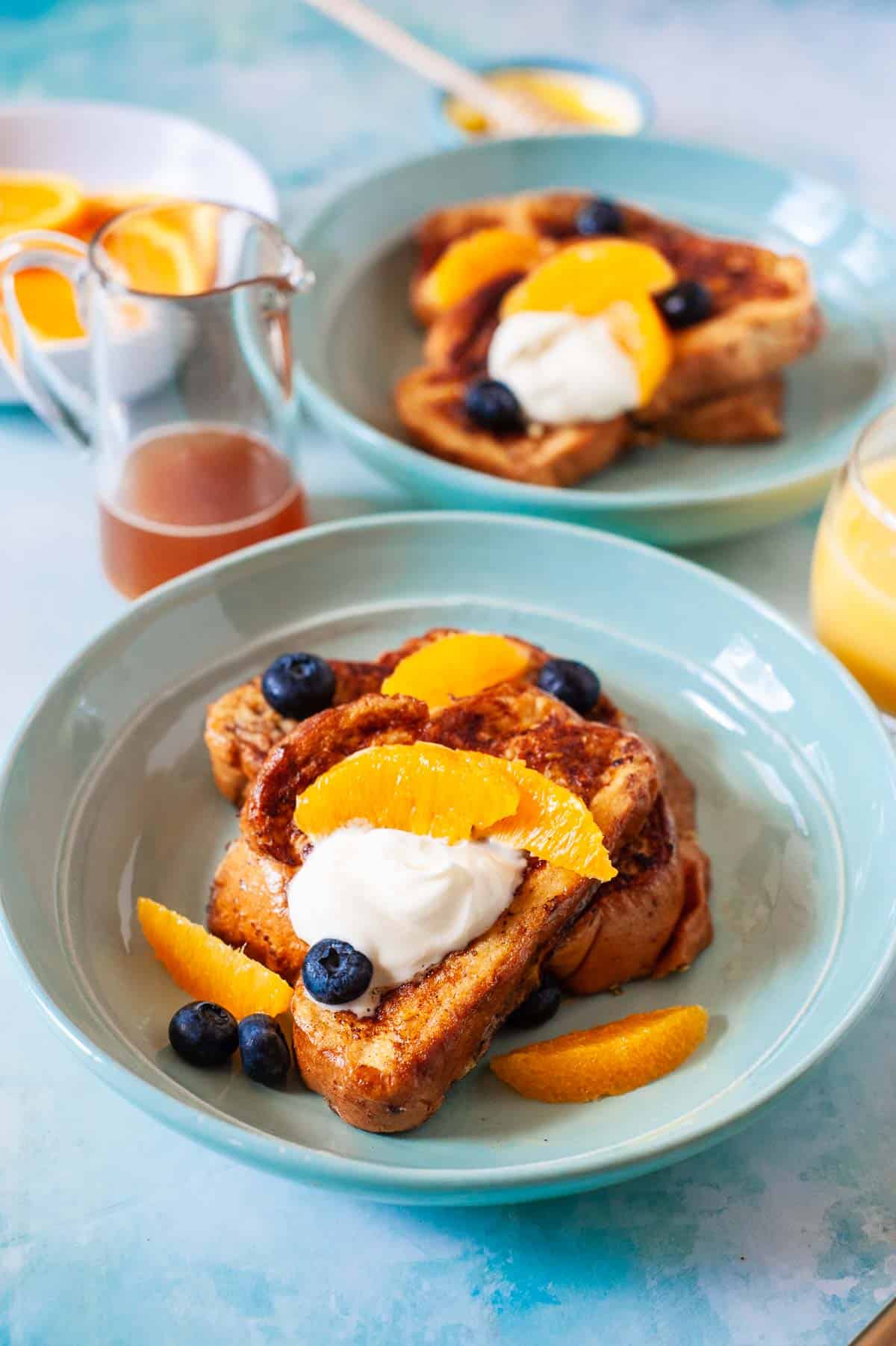 two plates of challah french toast topped with blueberries, oranges and creme fraiche..