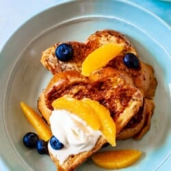 two slices of challah french toast topped with blueberries, orange slices and creme fraiche.