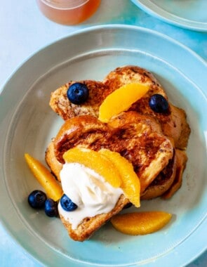 two slices of challah french toast topped with blueberries, orange slices and creme fraiche.