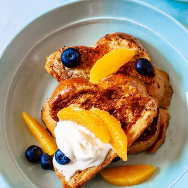 two slices of challah french toast topped with blueberries, orange slices and creme fraiche.
