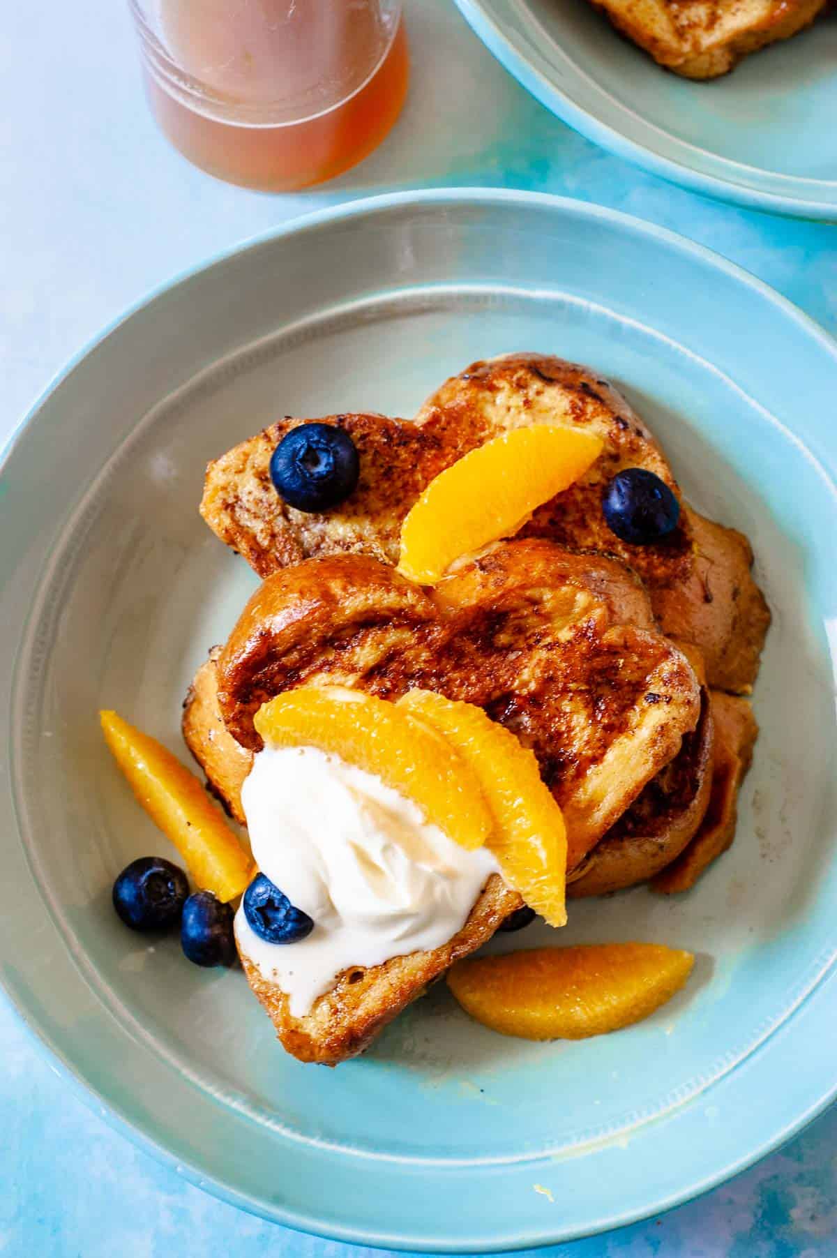 two slices of challah french toast topped with blueberries, orange slices and creme fraiche.