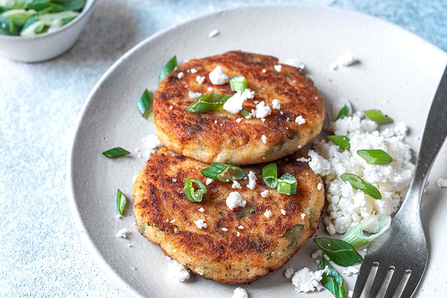 two potato pancakes with feta cheese and a fork on a plate.