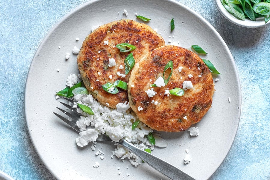 close up of two mashed potato pancakes on a plate with a fork.