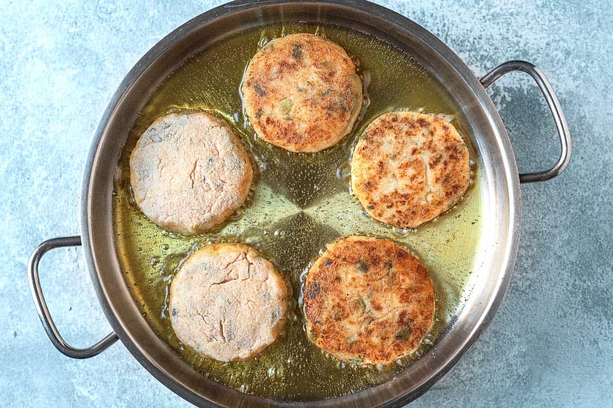 Five mashed potato pancakes frying in a pan.