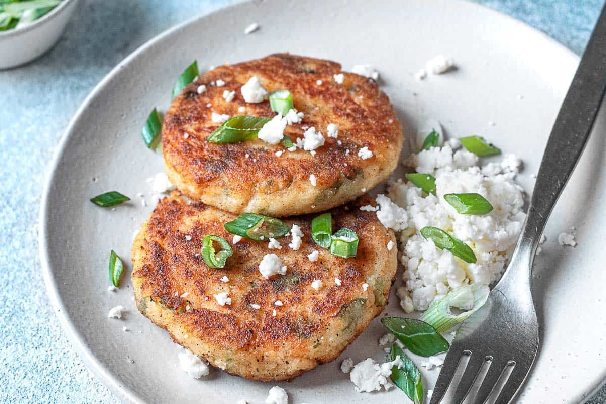 Two mashed potato pancakes on a plate with a fork.