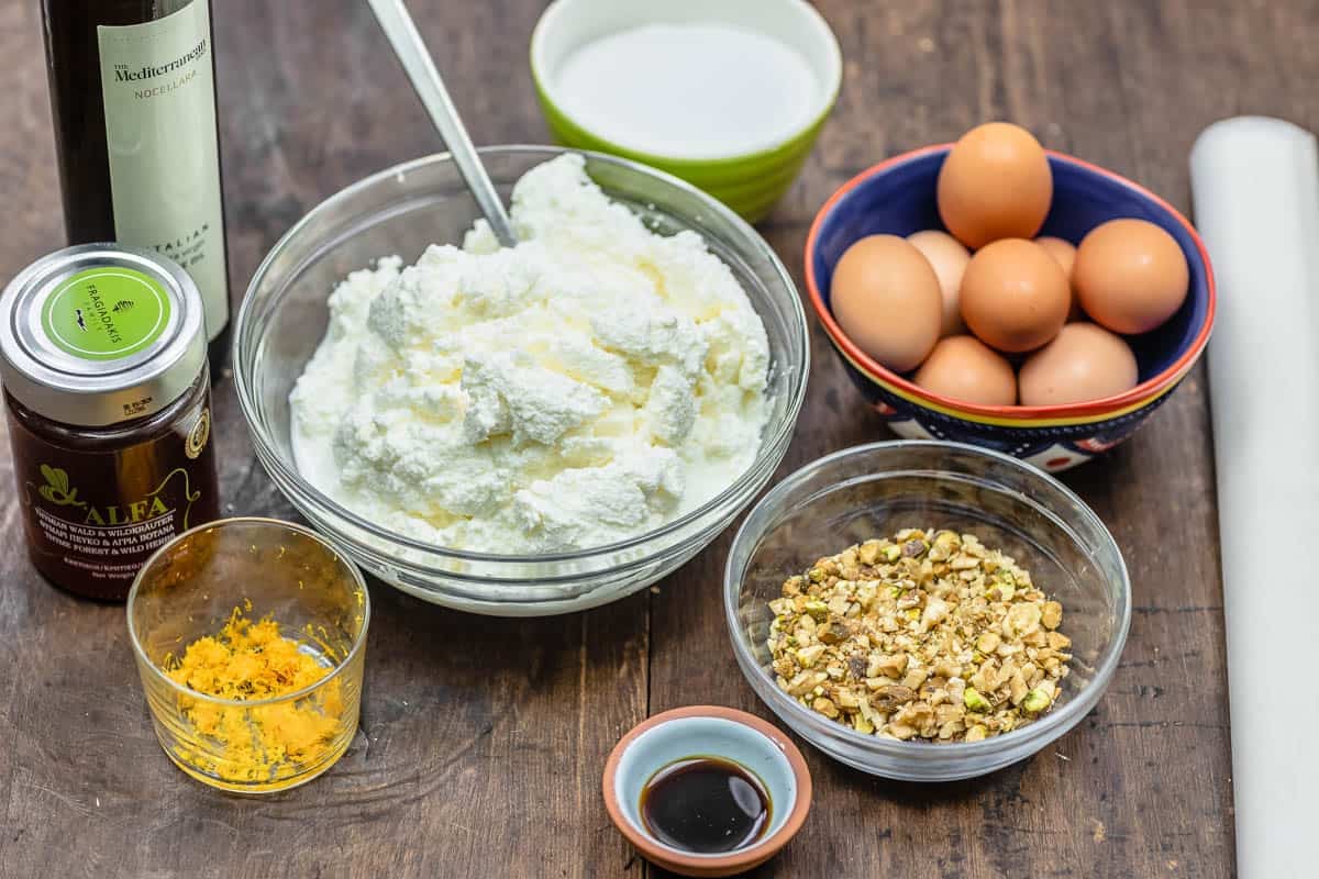 ingredients for baklava cheesecake including honey, orange zest, olive oil, ricotta cheese, sugar, eggs, nuts and vanilla.