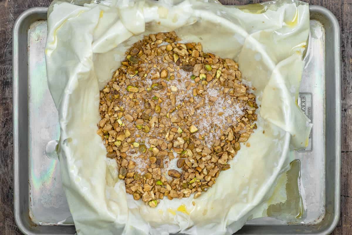 a layer of phyllo dough in a pan with a layer of nuts on top.